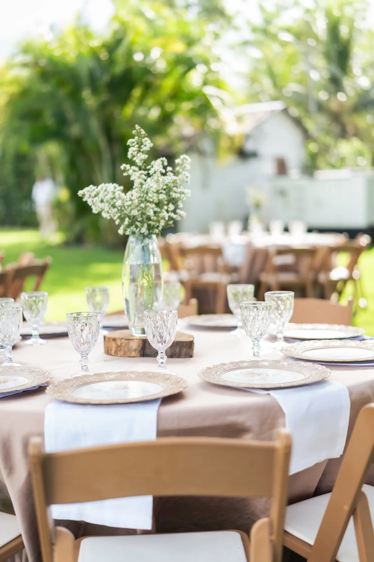 Mesa al aire libre con flores blancas, platos y sillas de madera